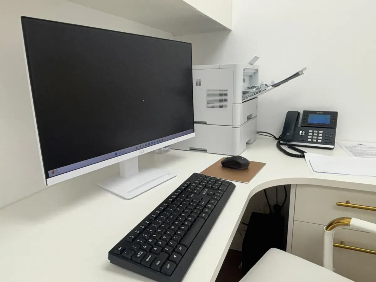Computer monitor, keyboard, desk phone and a printer set up on a corner desk